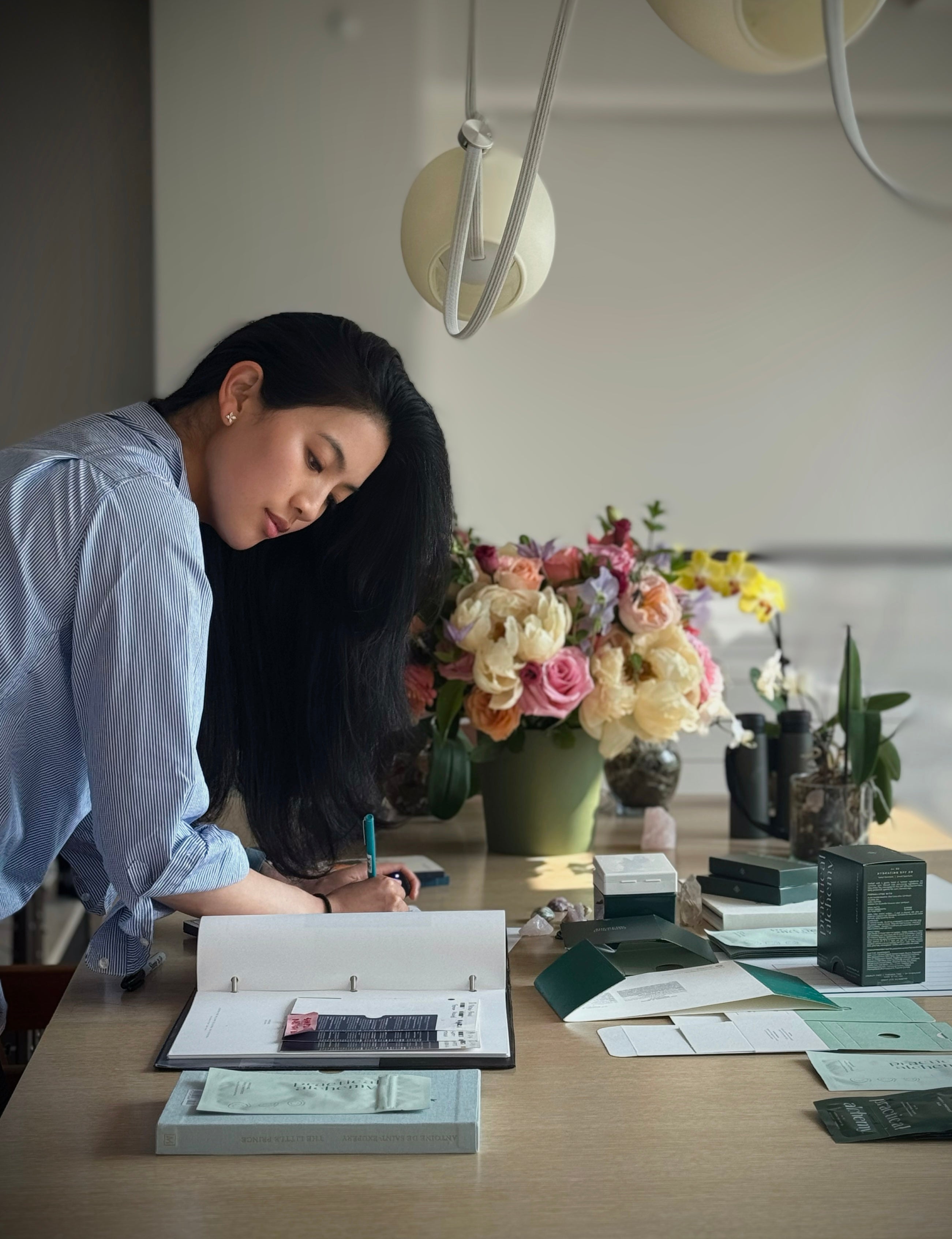 Practical Alchemy founder Doris working at a desk with books and flowers in a home office setting