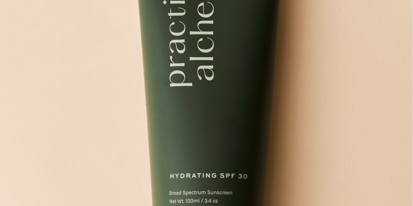 Green tube of Practical Alchemy hydrating SPF 30 sunscreen on a beige background