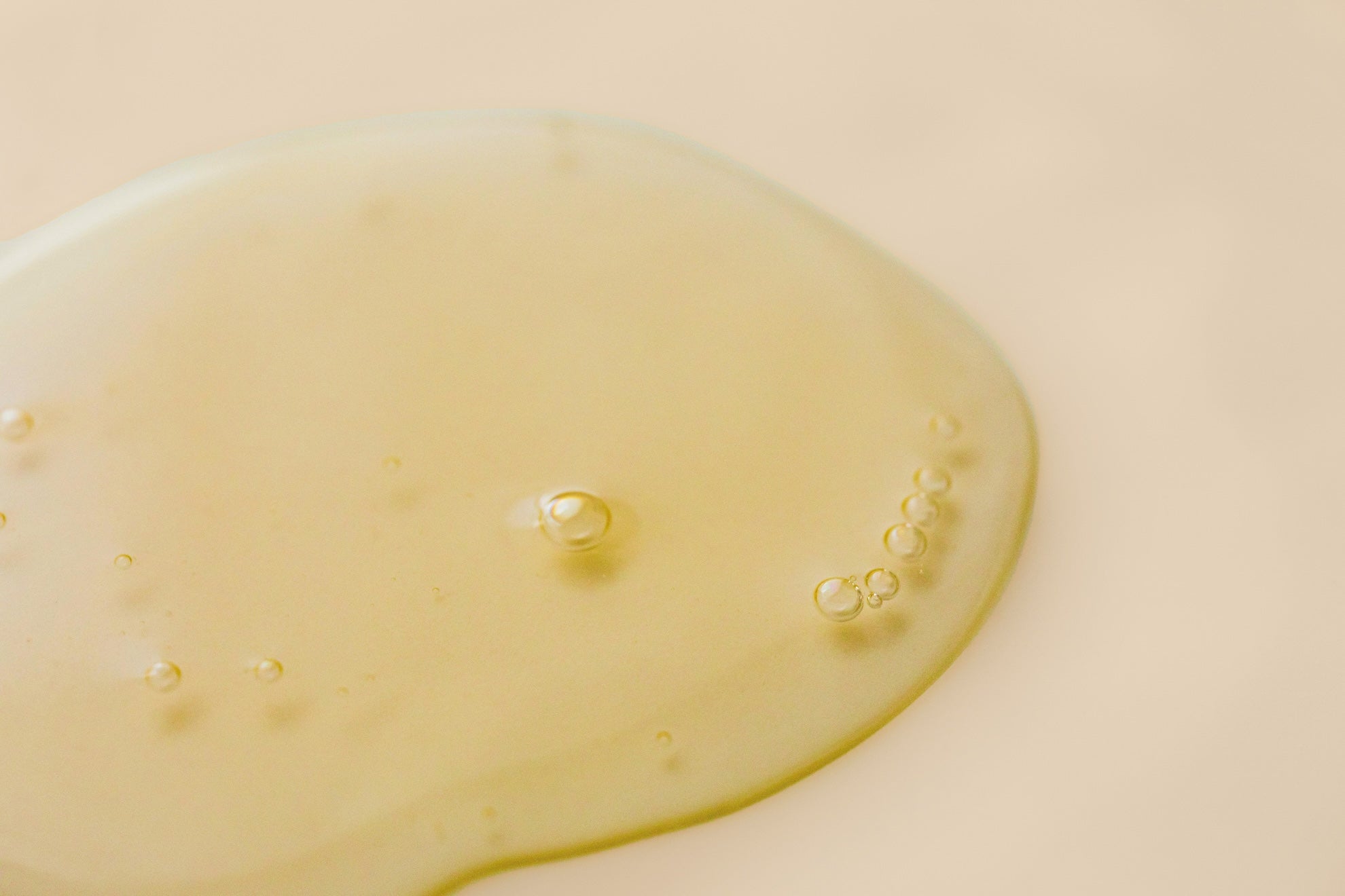 Jojoba oil with small bubbles sitting on a beige surface