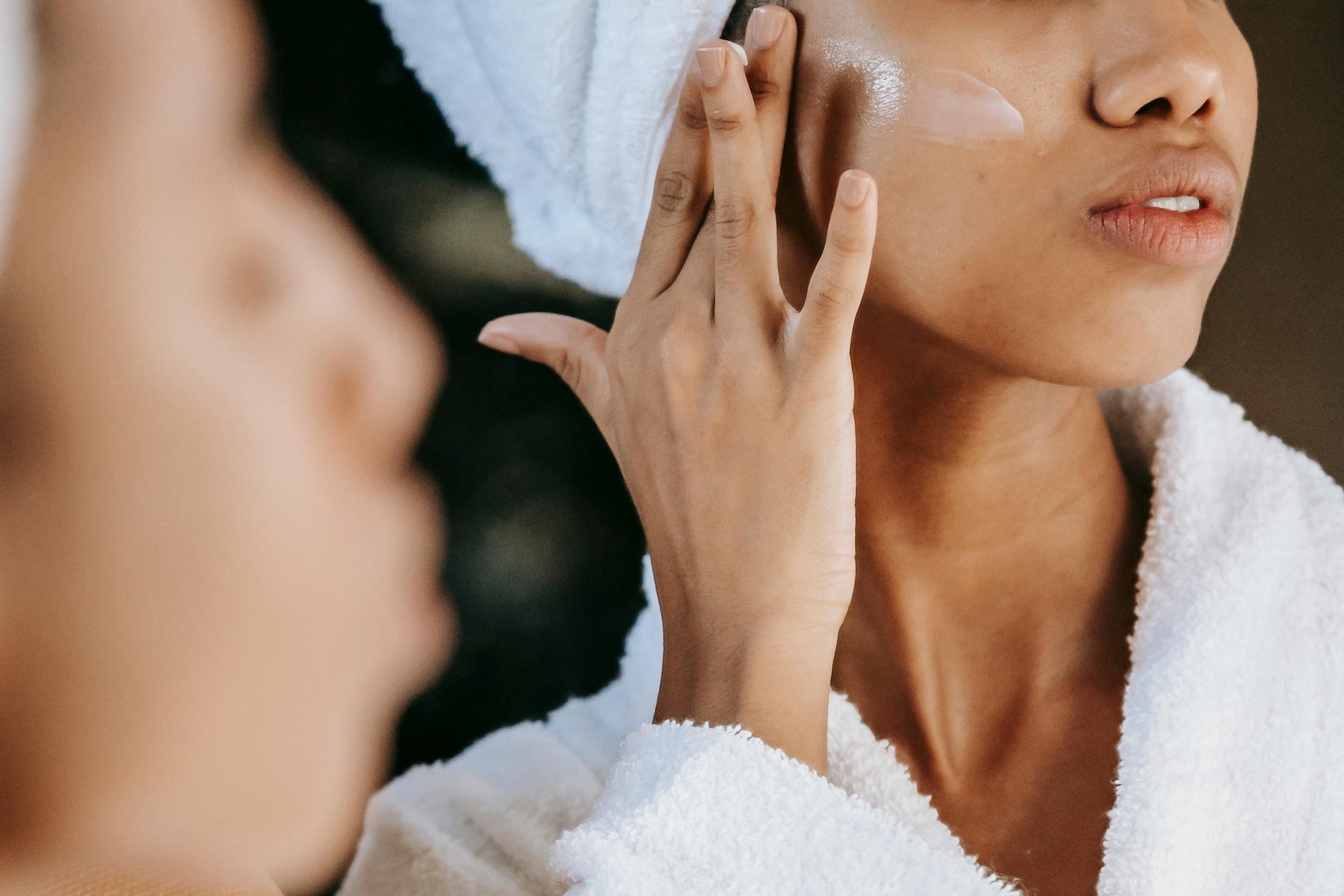 African american woman in bath robe spreading white cream on cheekbone