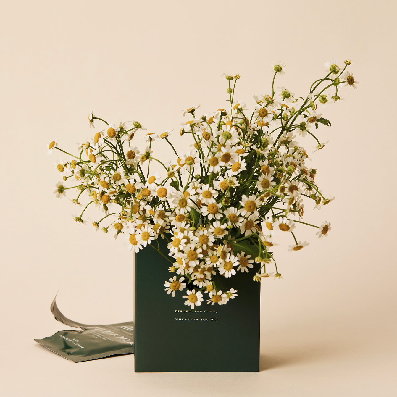 Bouquet of flowers in a green box with text on a beige background in front of an open Purify + Protect Duo sachet