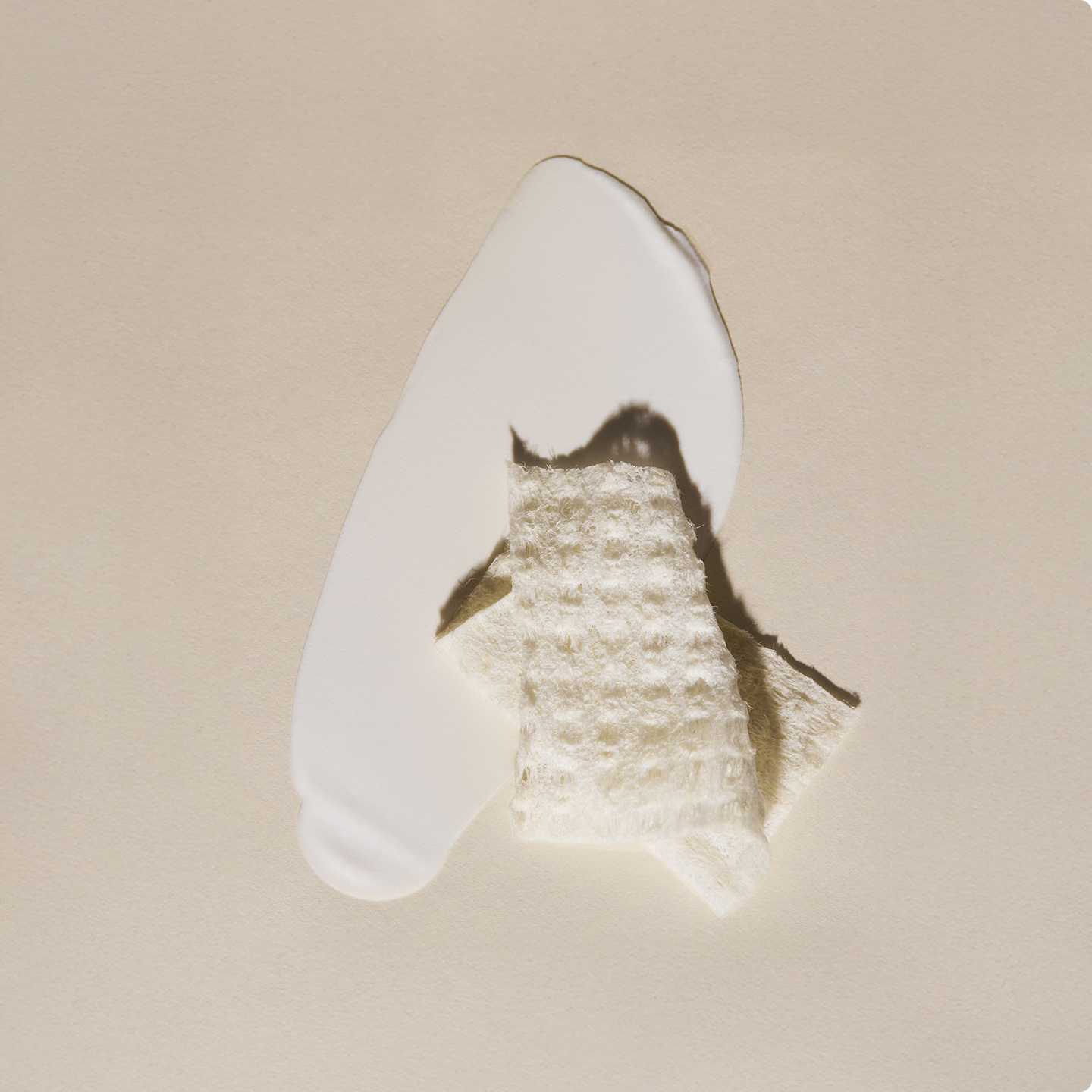 Smear of Hydrating SPF 30 sunscreen with a folding Purifying Cloth on top on a beige background