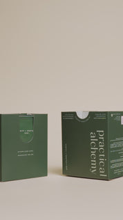 Female hands grabbing an open green box of Purify + Protect sachets and placing the inside of the lid of the green box. 